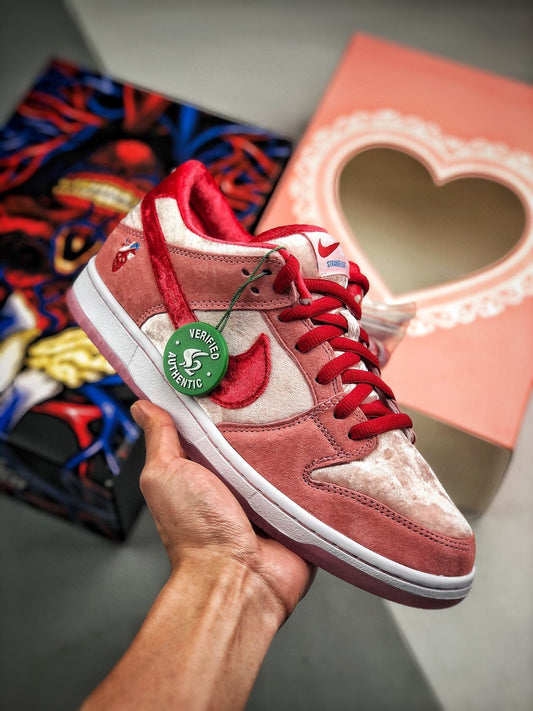 Red and white sneaker Nike SB Dunk Strange Love with a heart-shaped box and colorful packaging in the background.